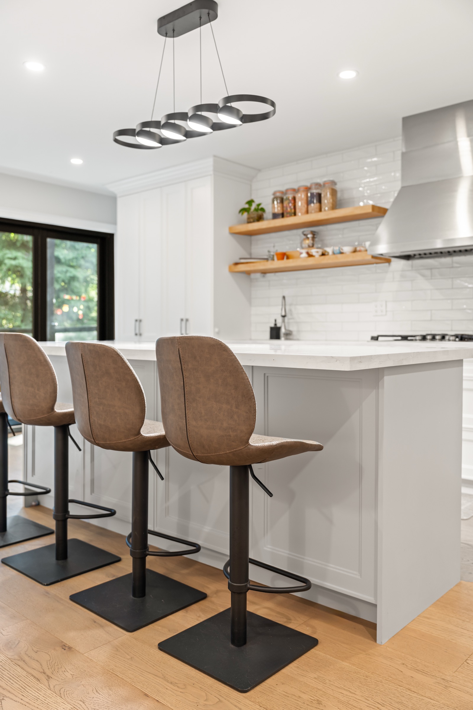 Island seating beside white cabinetry, open shelves and the cooking area in a completed Capable kitchen